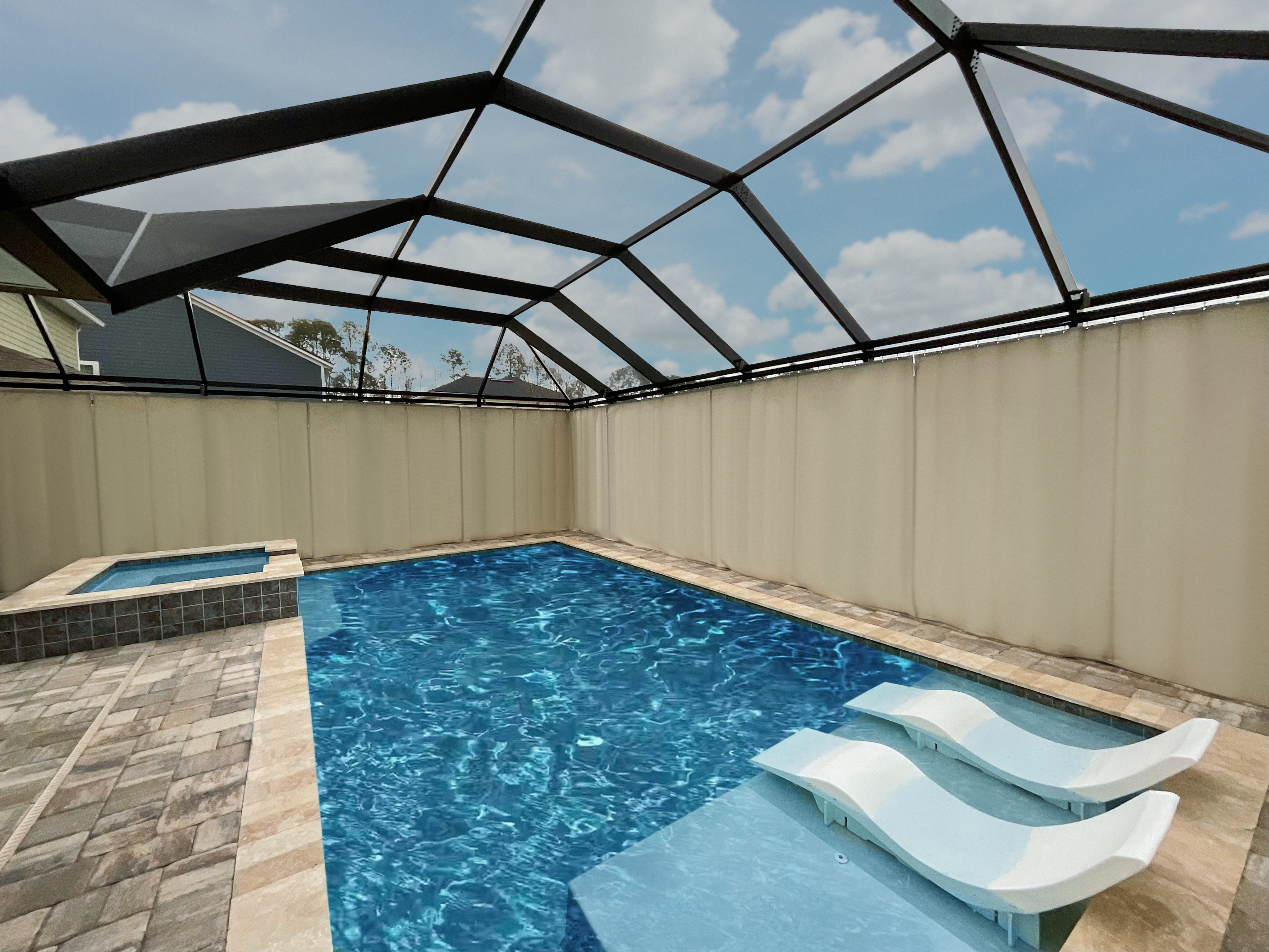A pool deck with Privacy on Demand privacy curtains attached to the perimeter of the pool cage.