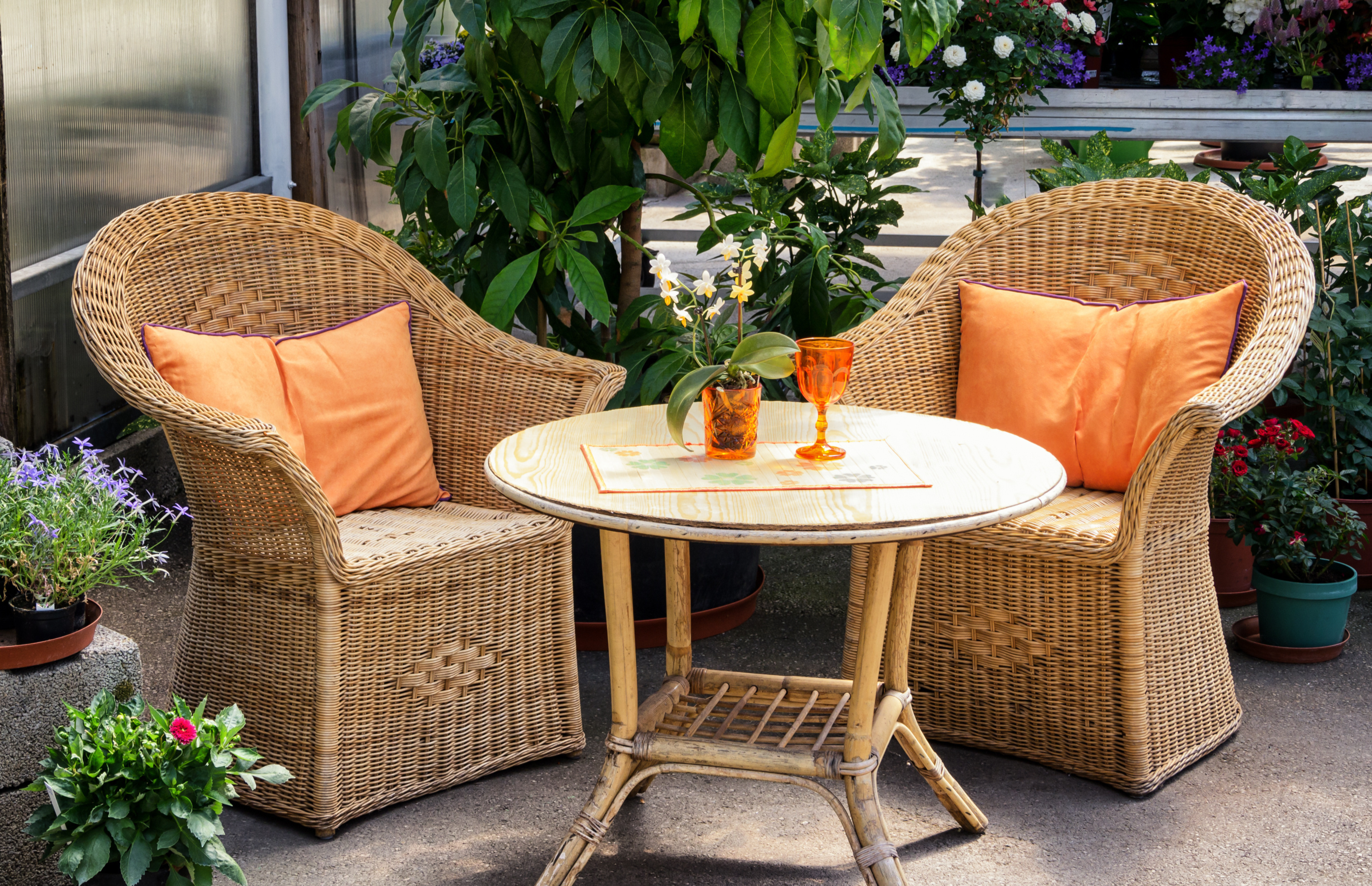 Two chairs and a table on this patio are surrounded by beautiful plants and flowers.