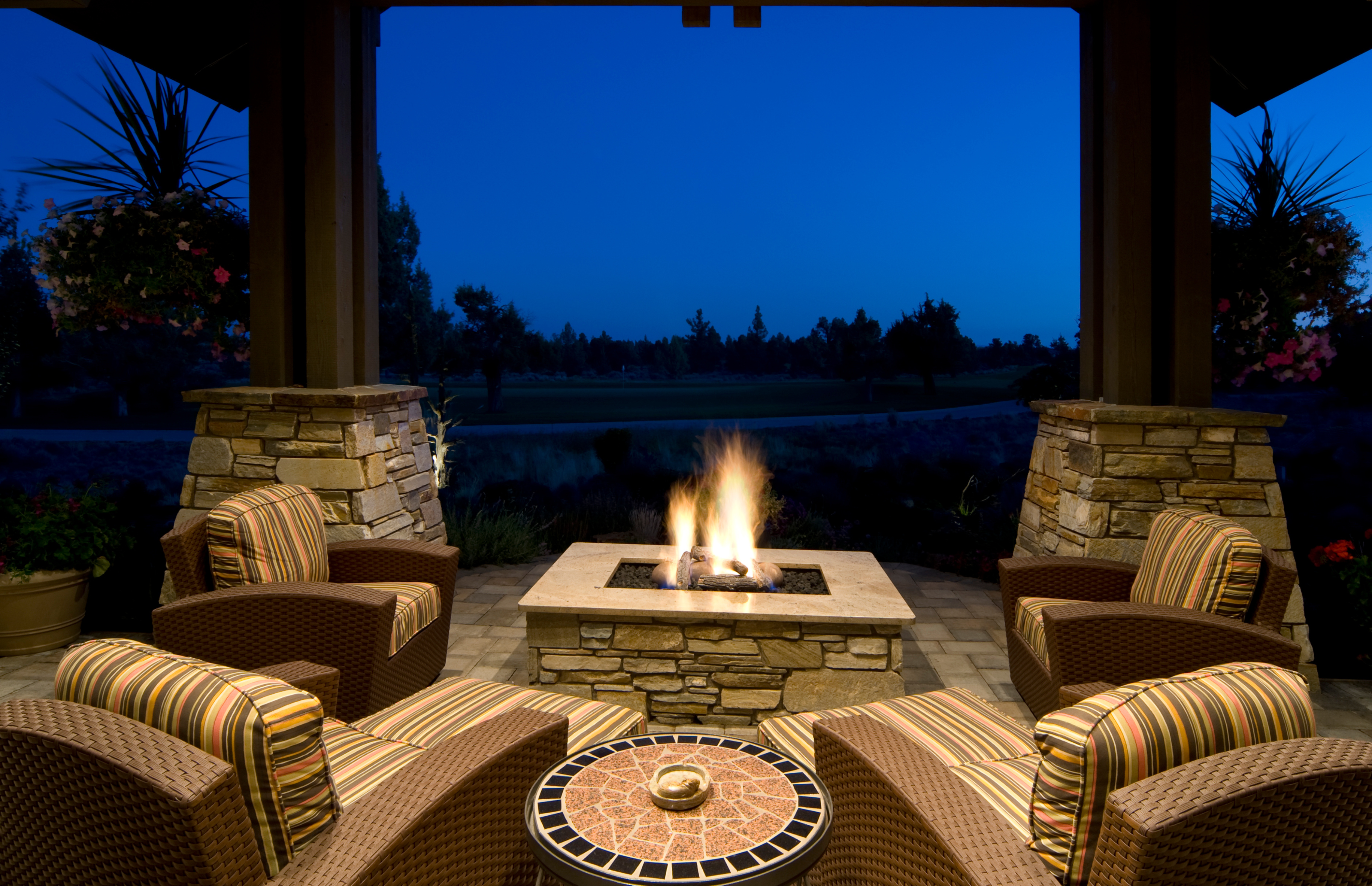 A fire pit is in the center of a patio surrounded by big armchairs just waiting for people to come and sit in them.