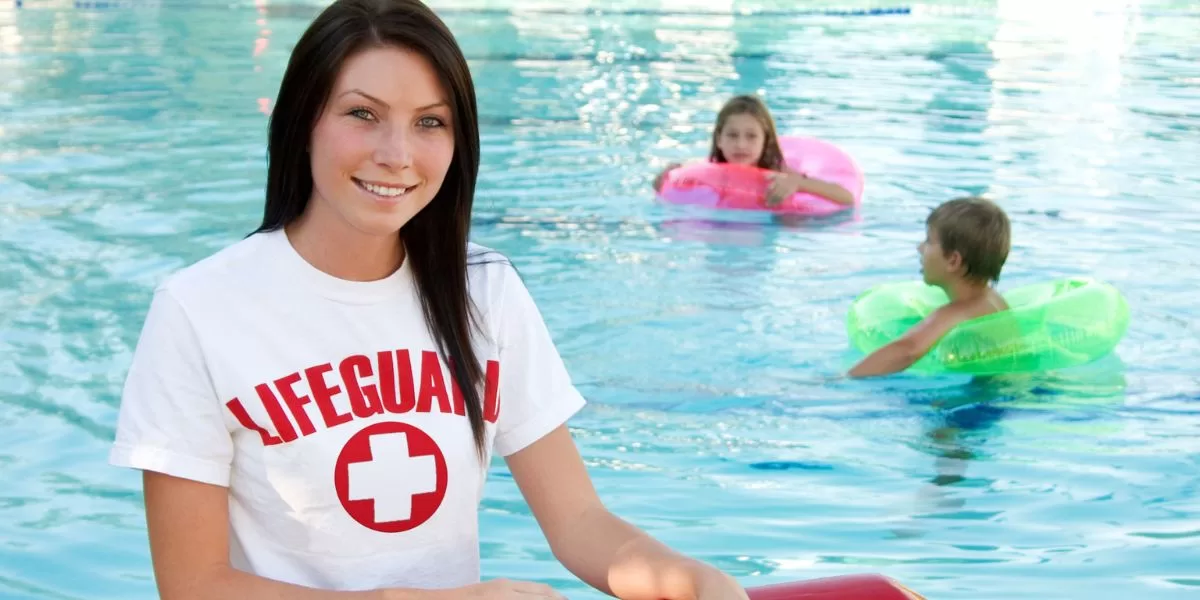 A lifeguard supervises two children as they swim in the pool.