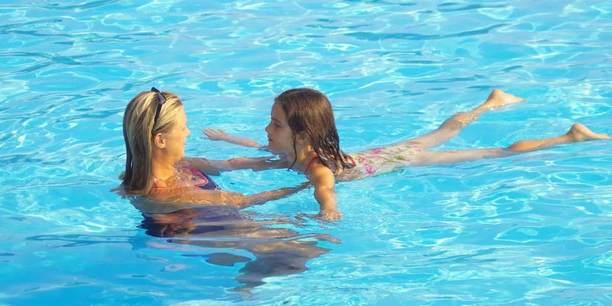 a woman is teaching her daughter how to float in a swimming pool. 