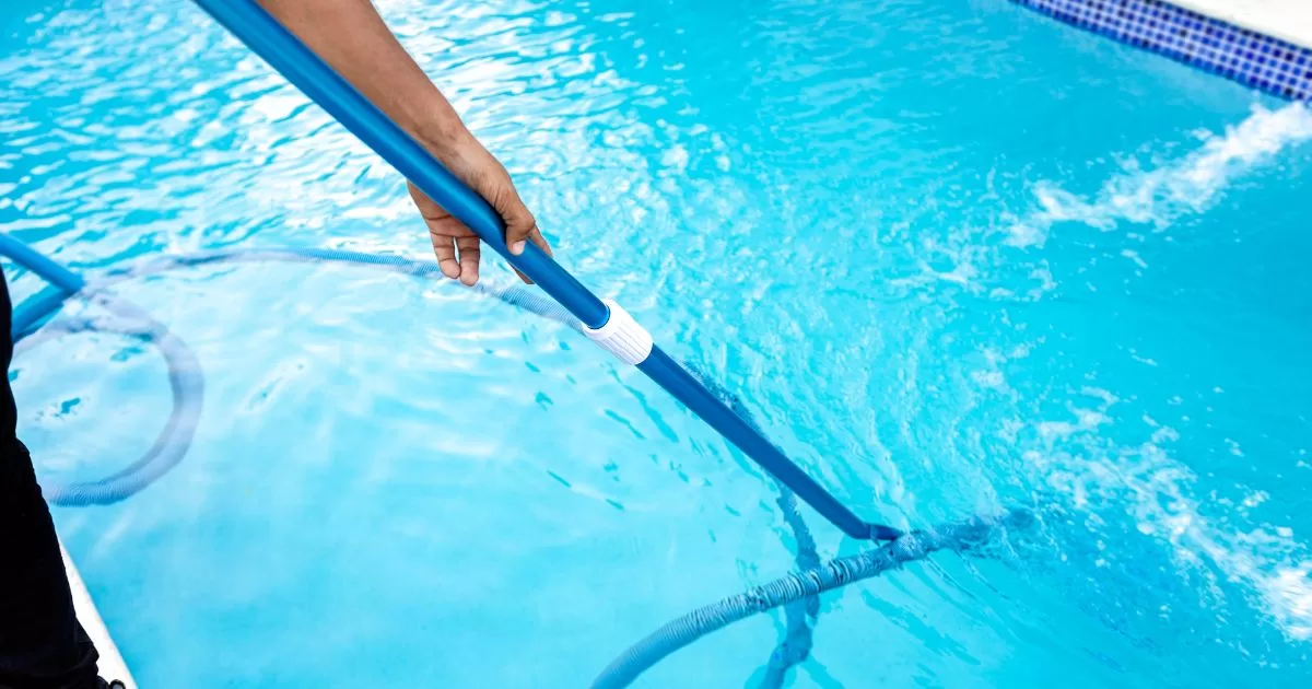 A man is cleaning his pool with a pool vacuum and skimming net.