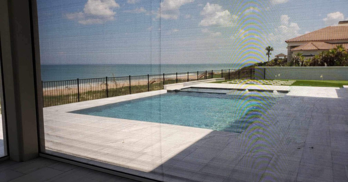 A retractable screen is down and through it we can see the beautiful view of a pool right on the ocean.