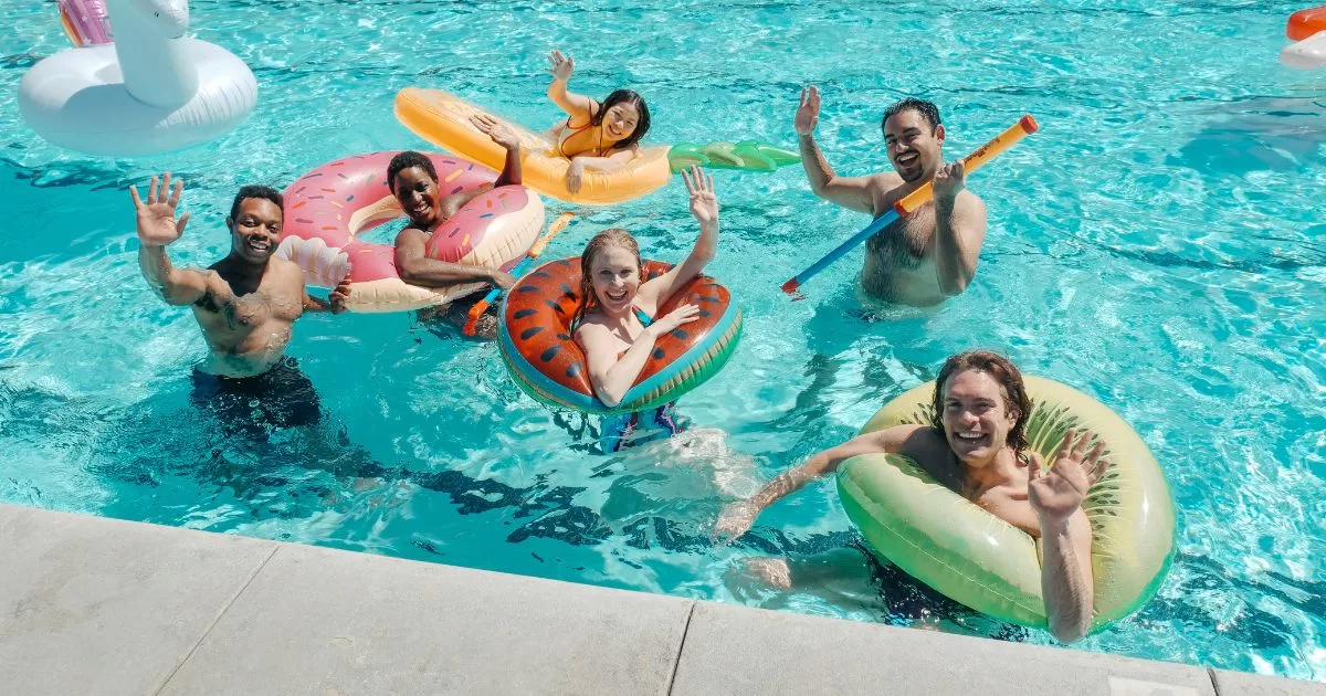 A group of people waves as they enjoy playing with pool floats and toys in their pool during fall.
