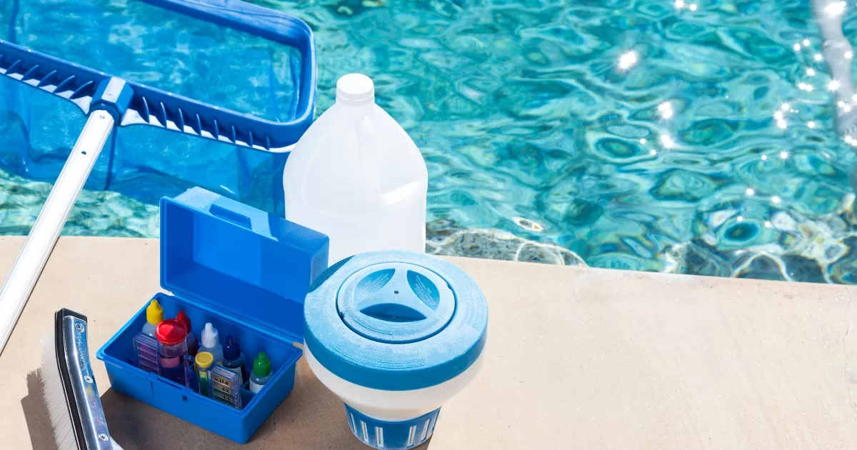 Pool chemicals, a strainer and other cleaning tools are laid out beside a beautiful pool that is getting ready for spring. 