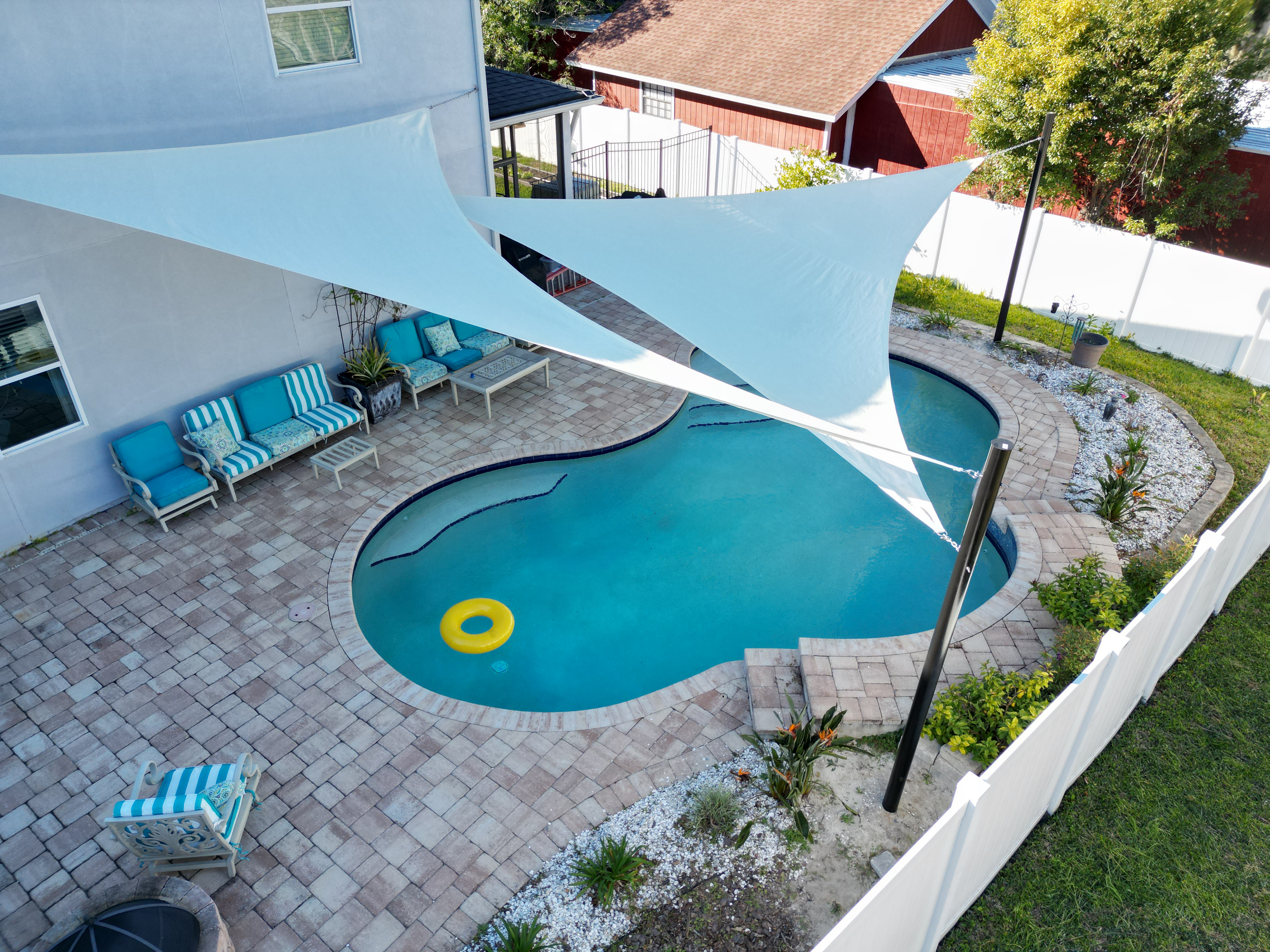 Two beautiful triangle shade sails soar over top of a backyard pool, keeping our the direct sun.